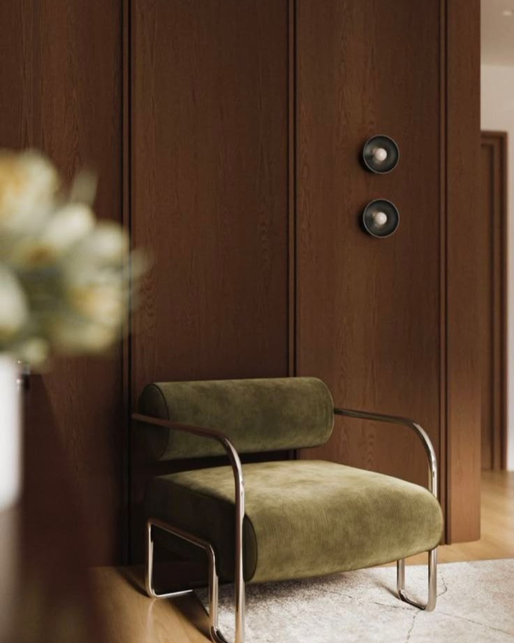 Fauteuil de velours vert à structure tubulaire devant des boiseries sombres