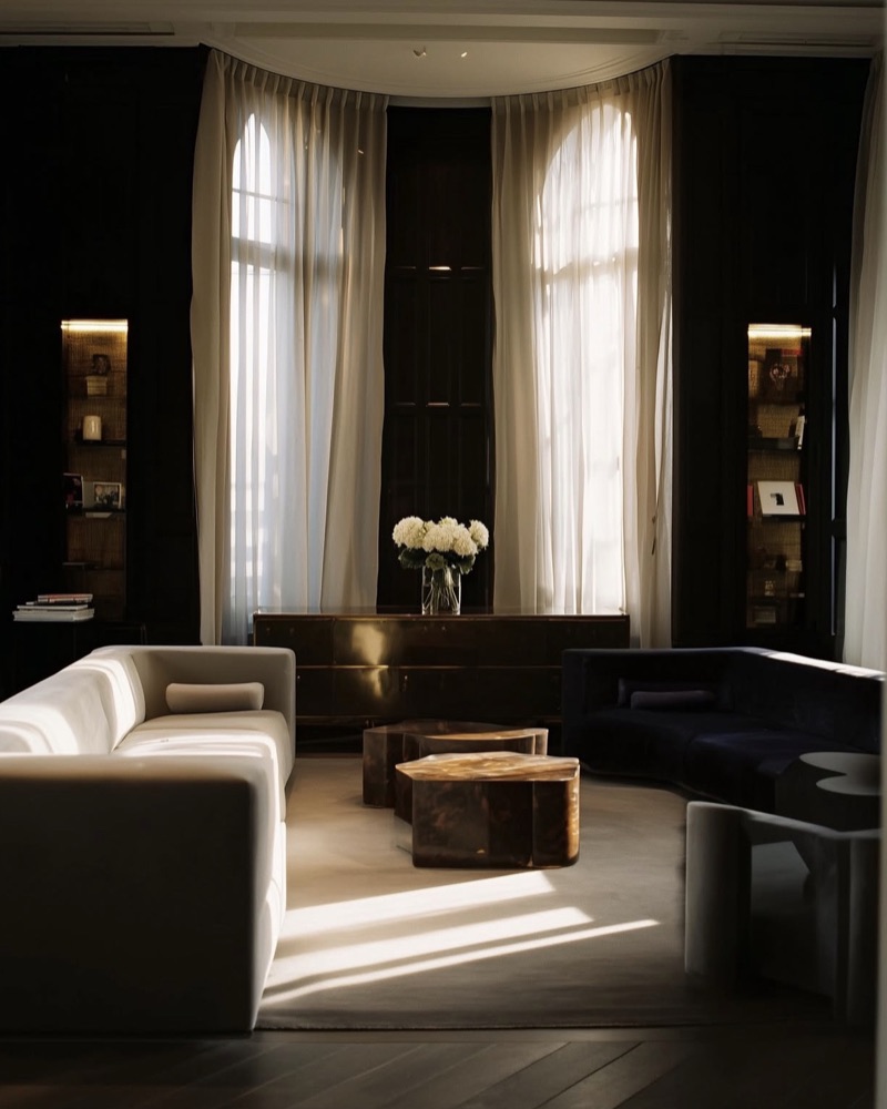 Salon sombre, canapé clair et bouquet blanc devant les rideaux