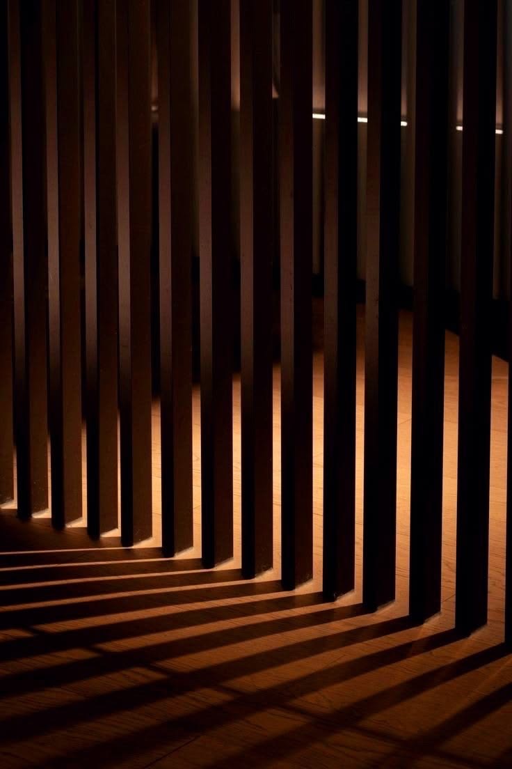 Claustra de lattes verticales et ses ombres portées, allongées sur un parquet chaud